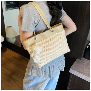 Detail view of woven straw tote bag texture with beige leather handle and bear charm