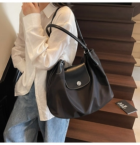 Close-up of black nylon tote bag featuring white contrast stitching and leather flap details