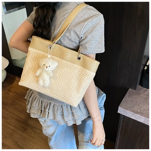 Detail of woven straw tote bag with khaki leather straps and cute plush bear charm
