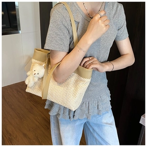 Side view of large woven straw tote bag with brown leather straps and bear charm
