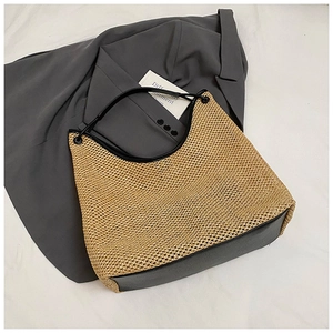 Detailed close-up of woven straw tote bag with black leather handles and trim
