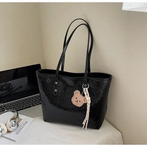Grande borsa tote nera con ciondolo a orsetto esposta accanto a laptop e libri d'arte