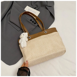 Detail of a large straw tote bag with brown leather trim and a cute plush bear charm