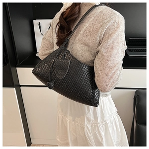 Shoulder view of a black woven leather tote bag for women in a minimalist indoor setting