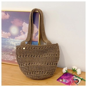 Detail of tan crochet woven handbag featuring intricate hollow patterns and a golden emblem