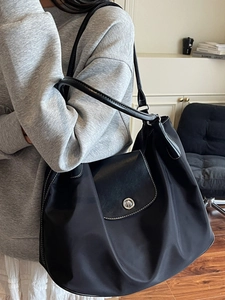 Large black nylon tote bag with leather trim and metal buckle shown on a female model