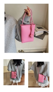 Detail der pinken Mini-Umhängetasche mit Lychee-Struktur und dekorativem Webknoten-Anhänger