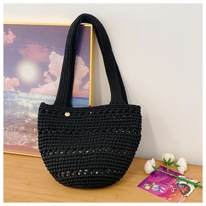 Detail of black crochet tote bag with circular golden metal logo on wooden table