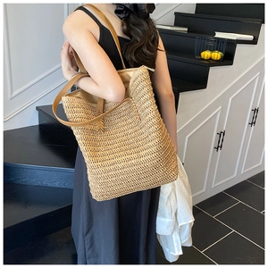 Close-up of woven straw tote bag with brown leather straps shown on a model