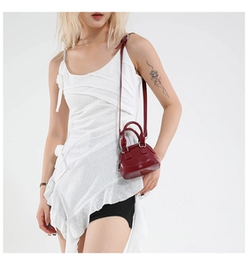 Detail of burgundy patent leather mini shell bag with silver hardware on a white dress