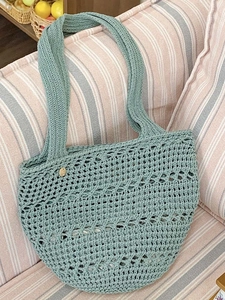 Green handmade crochet woven tote bag with open knit design on a pink striped sofa
