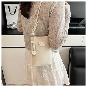 Détail du sac de téléphone en cuir PU crème avec sangle tissée, perle et breloques cœur