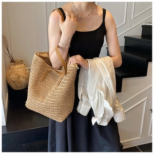 Detail of straw tote bag showing natural woven texture, leather handle and metal zipper