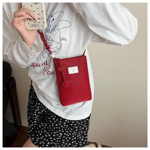 Détail du sac rouge avec logo nœud blanc, bandoulière perles et pendentifs cœurs