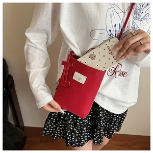 Détail d'un petit sac à bandoulière rouge avec écusson nœud blanc et breloques cœur