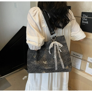 Close-up of black tote bag with silver butterfly patterns, lace bow, and pearl pendant detail