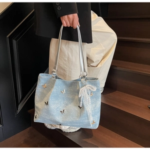 Detail of light blue denim tote bag with silver metal butterflies and lace pearl charm