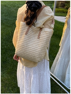 Detail of straw tote bag showing woven texture and brown leather strap with stitching