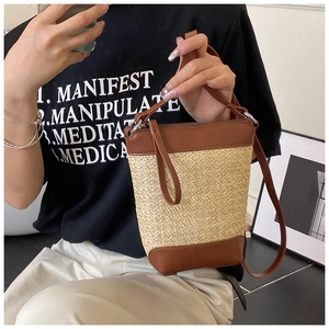 Detailansicht der gewebten Stroh-Eimertasche mit braunem Kunstlederbesatz und Riemen