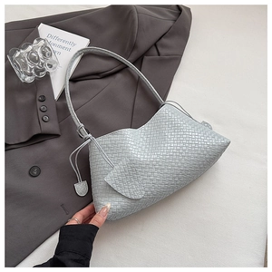 Detailed close-up of woven leather shoulder bag with side drawstring and woven pendants