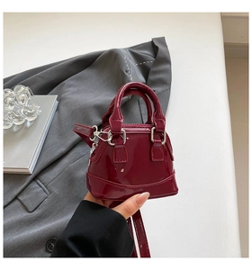 Detailed close-up of a mini dark red patent leather shell bag held in hand by a person