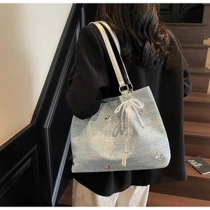 Detail of light blue tote bag with metal butterfly charms and lace bow on a model