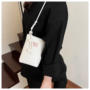 Détail du sac bandoulière blanc en PU avec étiquette nœud rose, perles et breloques cœur