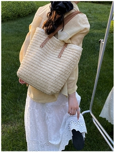 Detail of straw woven tote bag with brown leather handles and white reinforced stitching