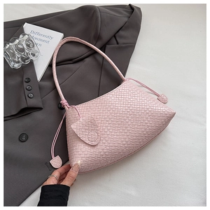 Detail of pink woven texture underarm bag with decorative side tassels on white bedding