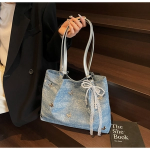 Detail of light blue denim tote with silver butterfly studs and a lace bow charm