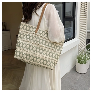 Close-up of woven straw tote bag with green geometric patterns and brown leather straps