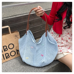 Close-up of light blue knit shoulder bag featuring colorful 3D bows and brown leather straps
