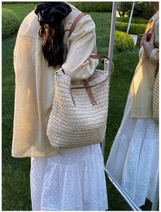 Detailed view of hand-woven straw tote bag with brown leather straps and cross-stitching