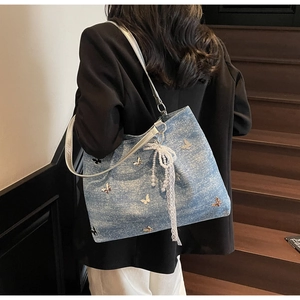 Detail of blue denim tote bag with 3D butterfly decor and pearl lace bow charm