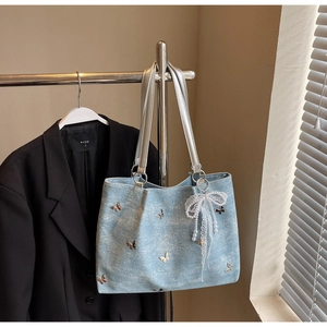 Close-up of light blue denim tote bag with butterfly embroidery and pearl charm