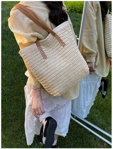 Straw tote bag with brown faux leather handles and white stitching detail on green grass