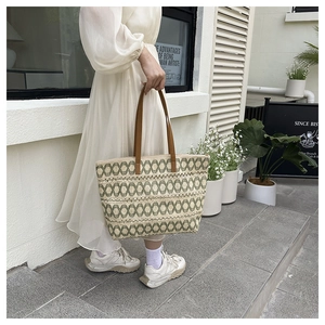 Detail of hand-woven straw tote bag with green geometric patterns and leather handles