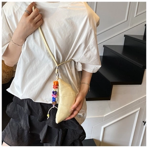 Close-up of cream croissant crossbody bag with quilted details and letter charm