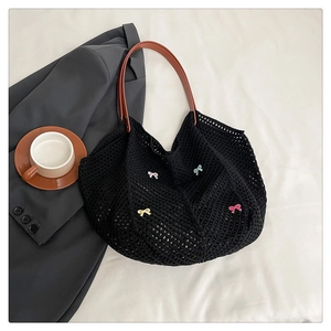 Detail of black woven tote bag featuring colorful crochet bows and brown leather handles