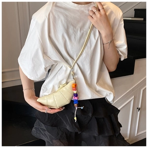 Detail of a beige croissant crossbody bag featuring quilted texture and colorful letter beads