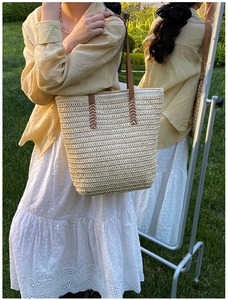 Detail of straw tote bag showing brown leather handles and decorative white cross stitching