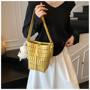 Detail of yellow hollowed-out bucket bag with laser-cut holes and plush pendant