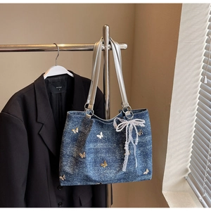Detail of blue denim tote bag with metallic butterfly accents and pearl lace charm