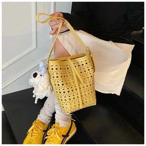 Detail of yellow hollow-out bucket bag with cute plush bear charm on a model