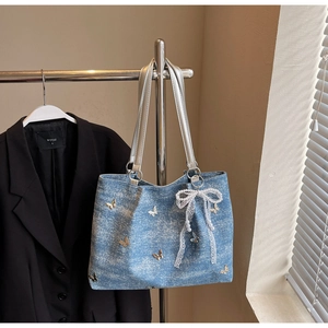 Detailed close-up of light blue denim handbag with metallic butterflies and pearl lace bow