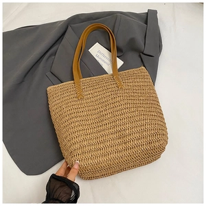 Detail of hand-woven straw tote bag with brown leather handles and reinforced stitching
