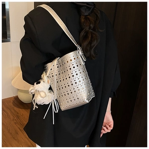 Detail of silver laser-cut bucket bag with plush dog charm and pearl bow accessory