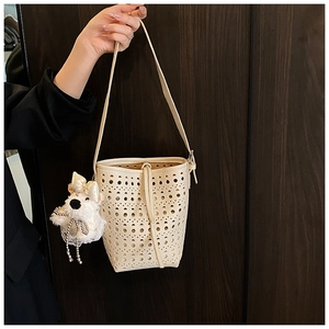 Close-up of cream hollow-out bucket bag with a cute white plush puppy charm accessory