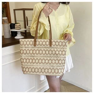 Detail view of woven straw tote bag featuring contrast leather straps and hollow patterns