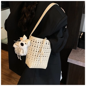 Detail view of cream-white hollow-out bucket bag with a cute plush dog pendant charm